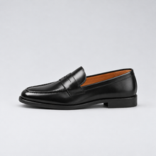 Black penny loafer, side view with generous margins on a light grey background
